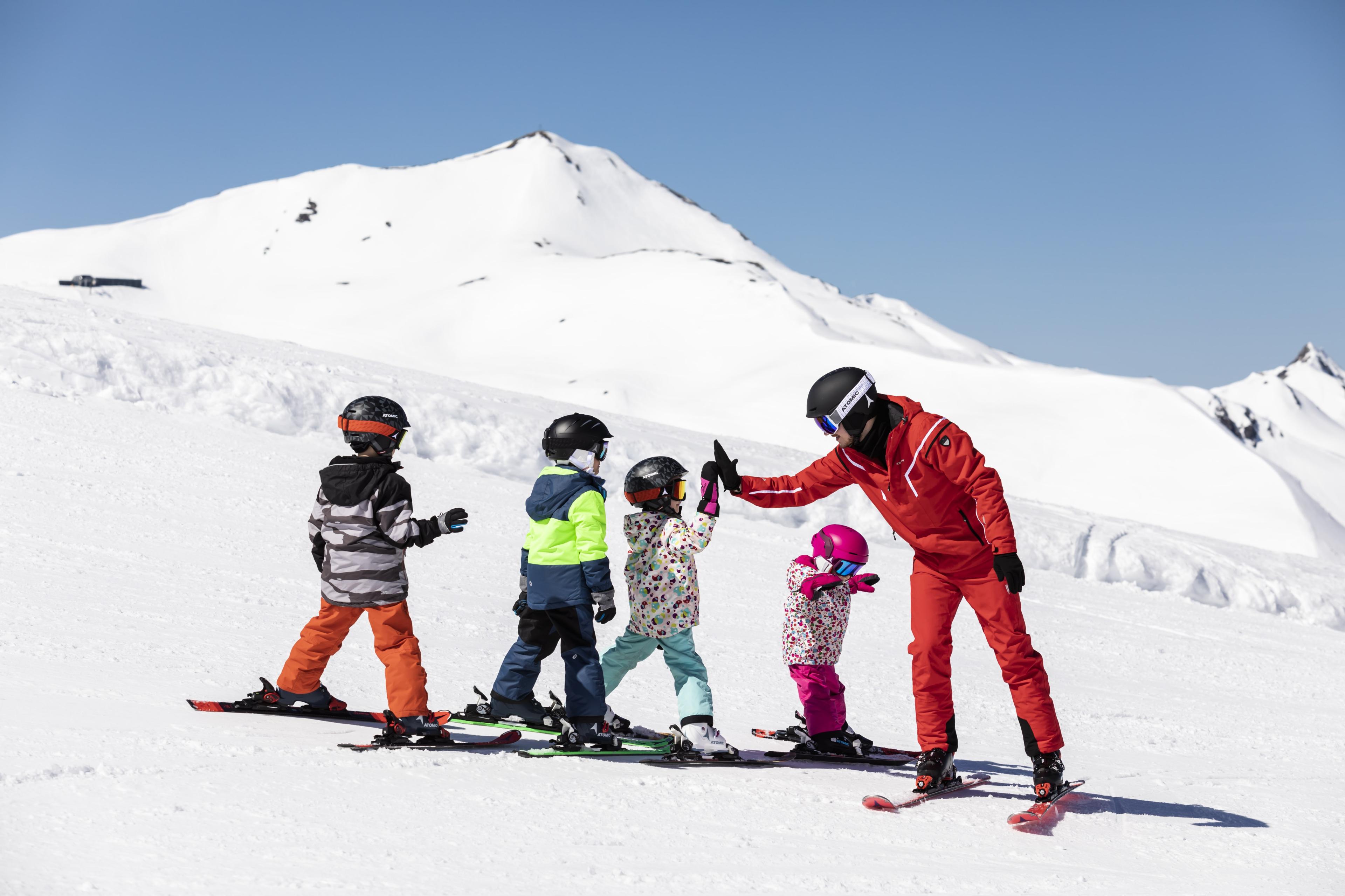 A ski instructor is high fiving the kids taking part in his group ski lessons.