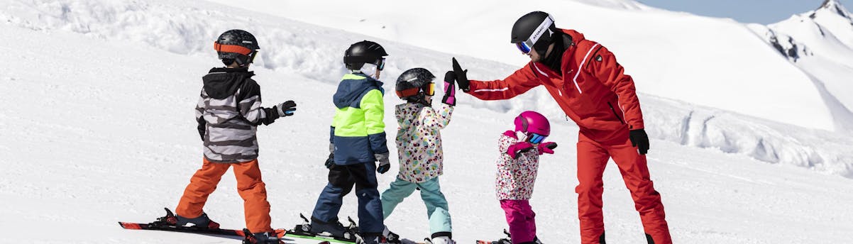 group-ski-lessons-SEM-hero1 Un instructor de esquí está chocando los cinco con los niños que participan en sus clases colectivas de esquí.