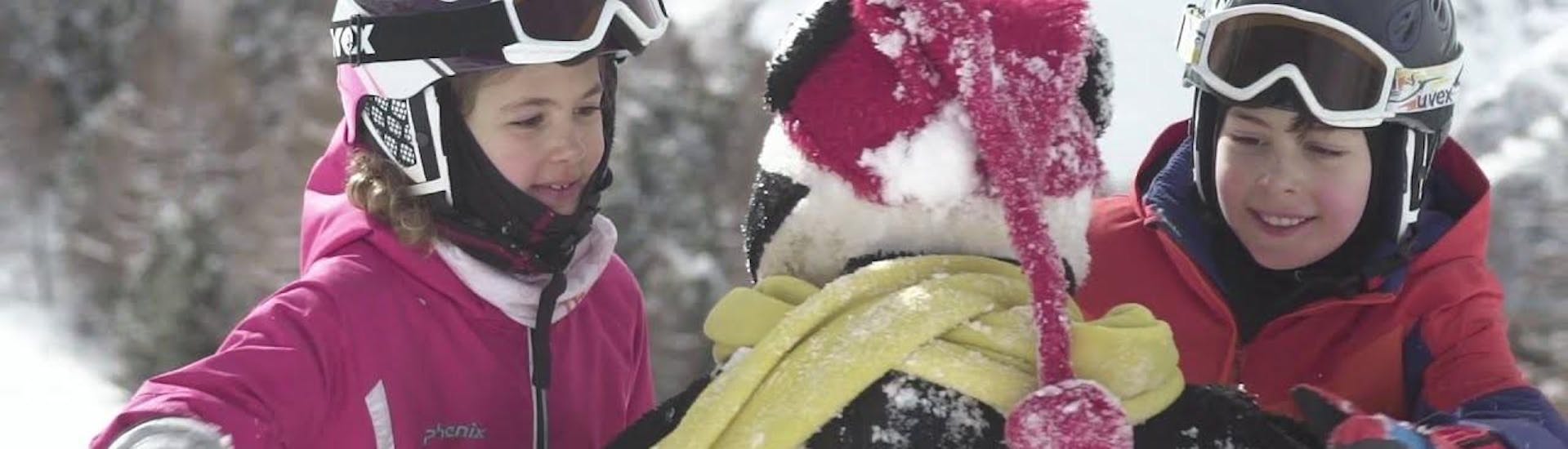 Two children hug the mascot Bobi after successful kids ski lessons with the Ski School Grächen.