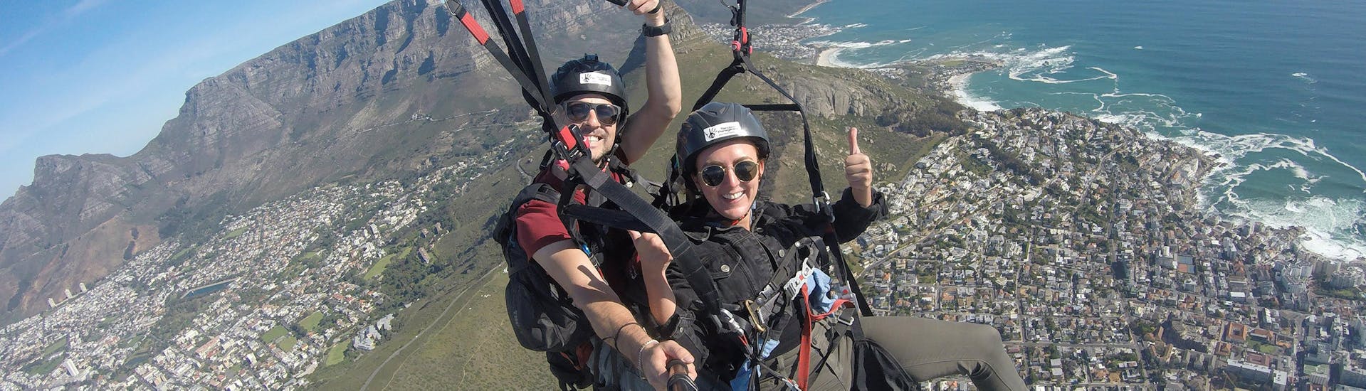 Happy woman flys with her tandem pilot over the city, enjoying the view of the sea and the mountains during paragliding in Cape Town with Hi5 Tandem Paragliding Cape Town.