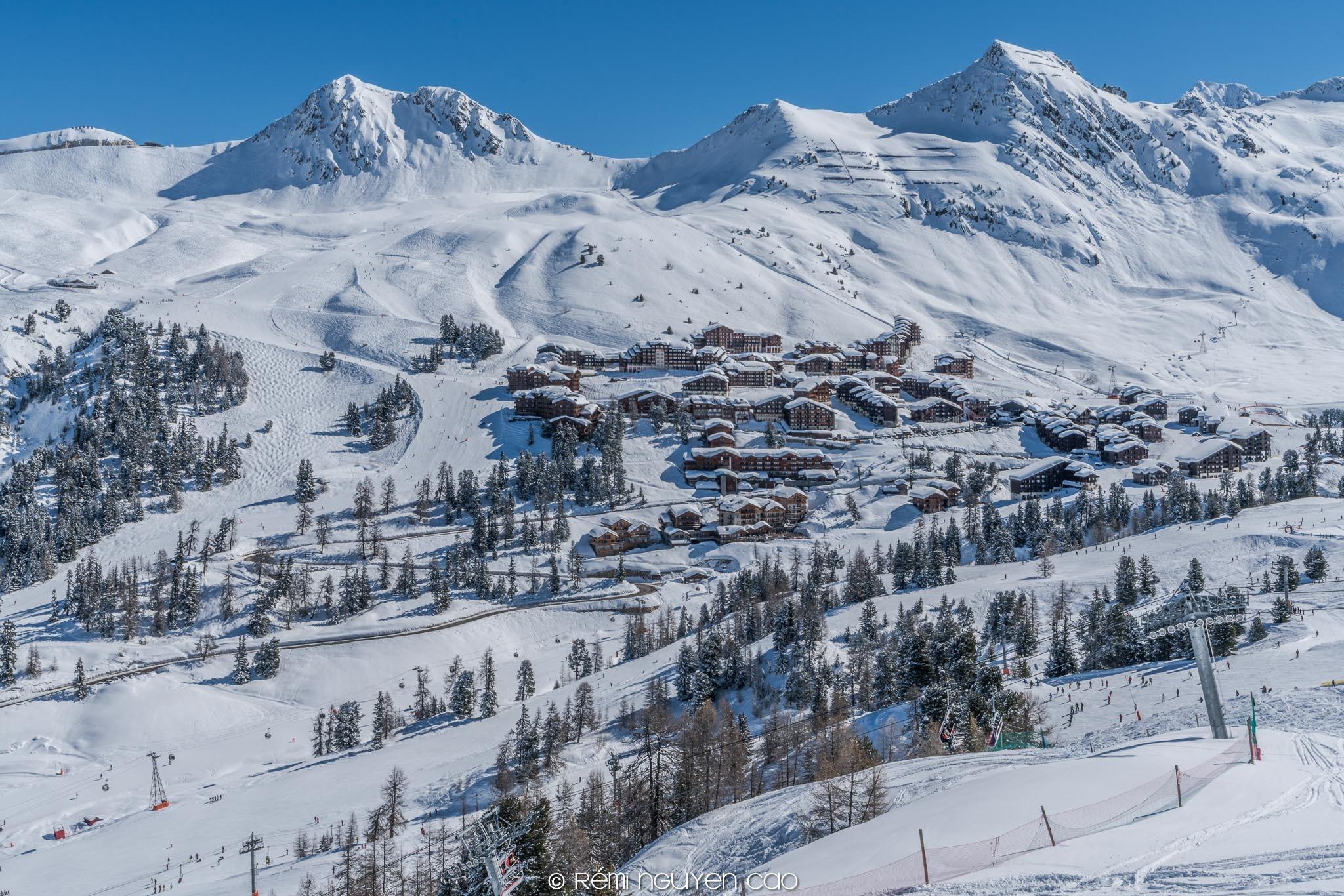 Het skigebied Belle Plagne in de verte met besneeuwde dennenbomen en chalets.