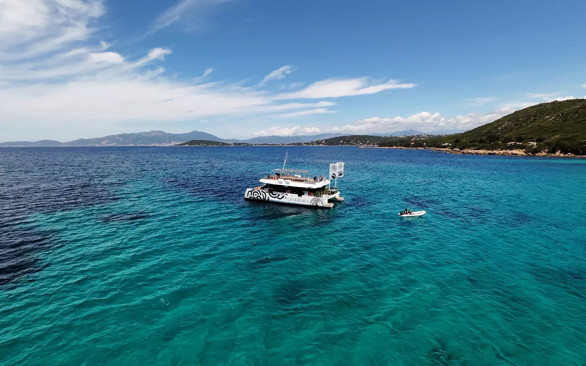 Il catamarano di Catabeach sulle acque turchesi della Corsica con la costa sullo sfondo.