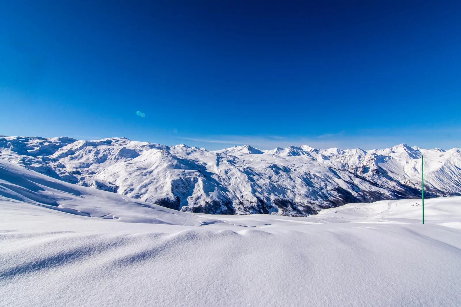 The snow-capped mountains of Saint Martin de Belleville resort with the Oxygene ski school under a turquoise blue sky.