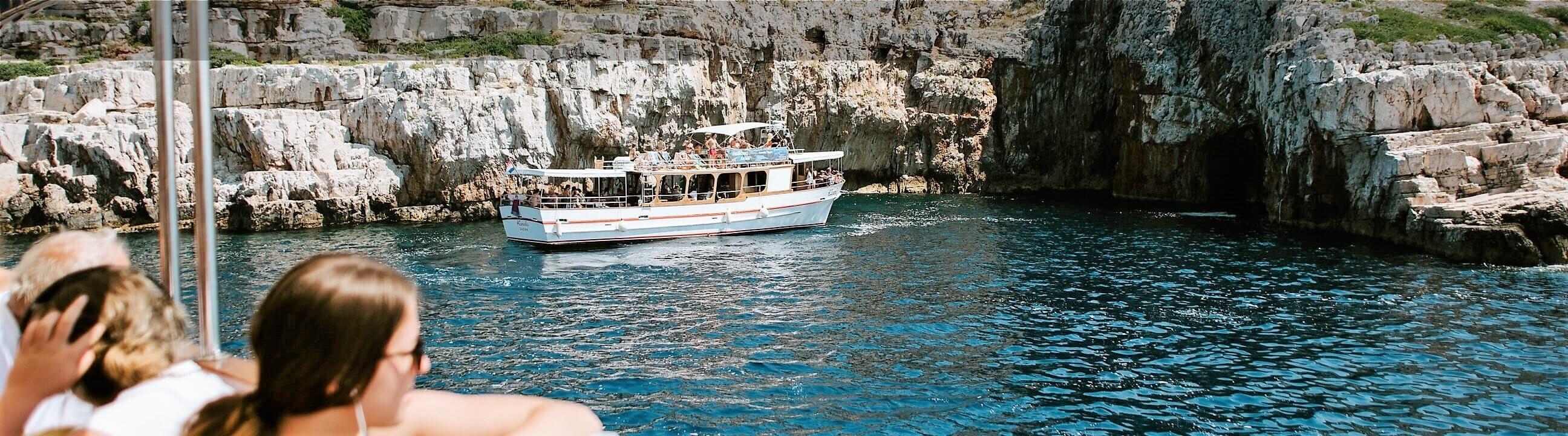 An image of a traditional wooden boat anchored in a bay surrounded by cliffs during a full day boat trip to National Park Kornati and Nature Park Telašćica from Kanela Tours.