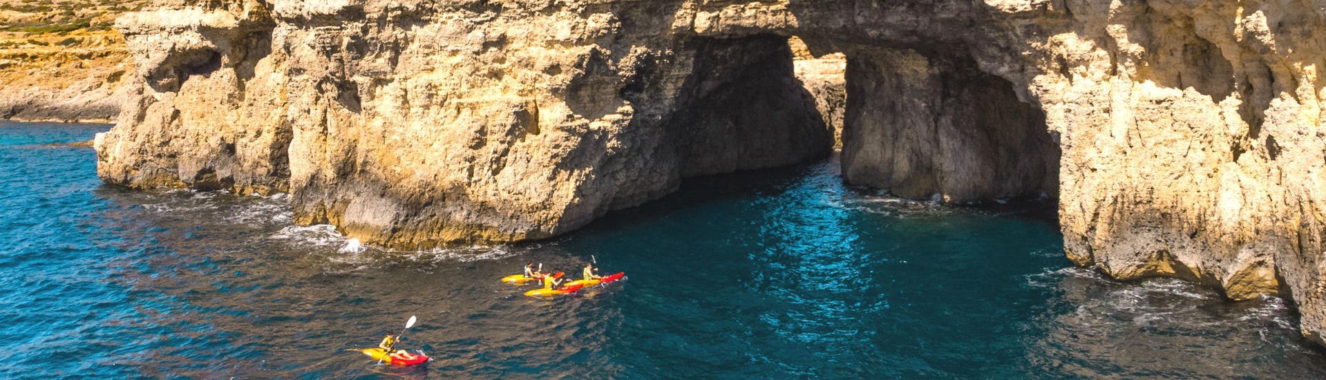A group of people is paddling into a cave while kayaking in Gozo.