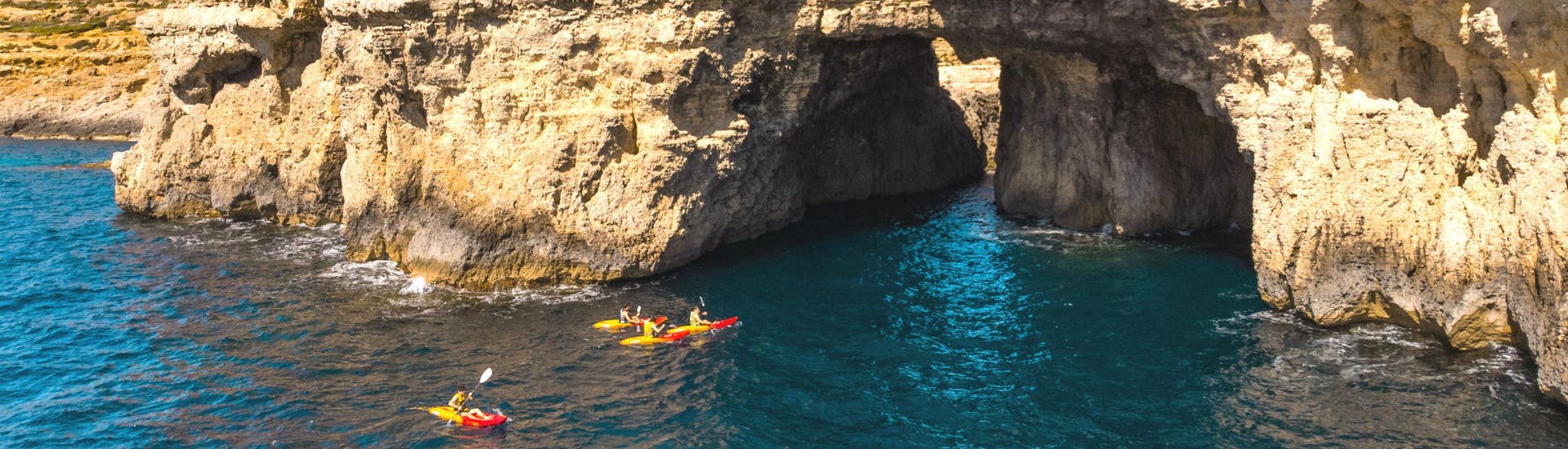 A group of people is paddling into a cave while kayaking in Malta.