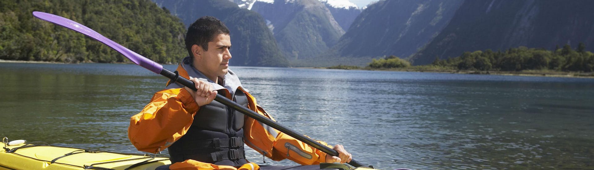 A young man is kayaking in the Milford Sound fjord and enjoying the spectacular scenery.
