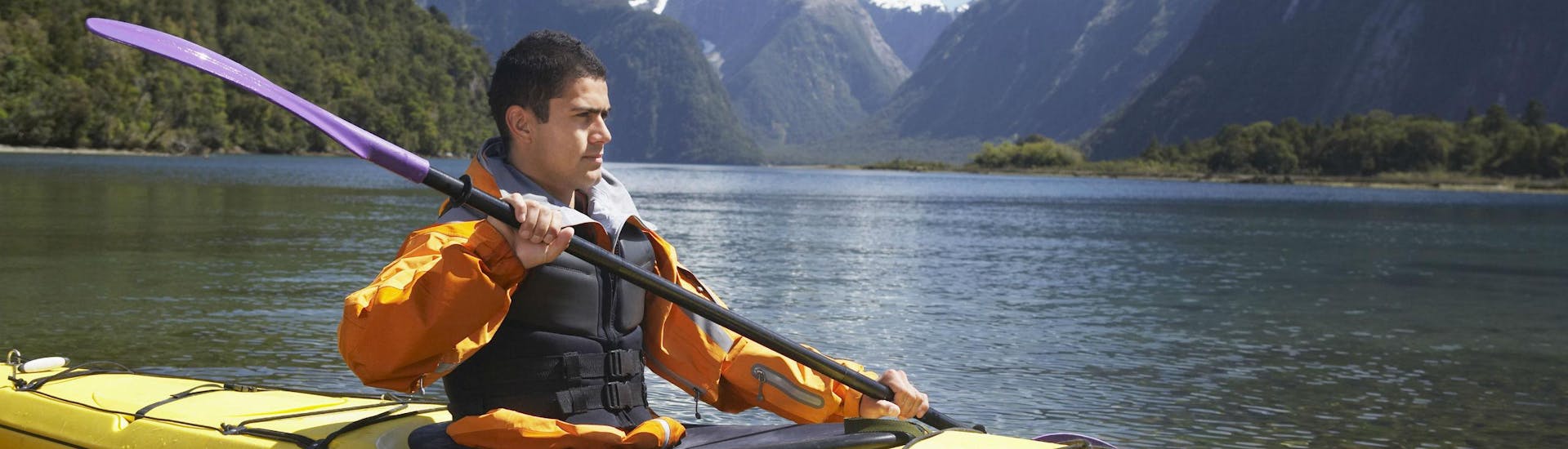 A young man is kayaking in Milford Sound and enjoying the spectacular scenery of the fjord.