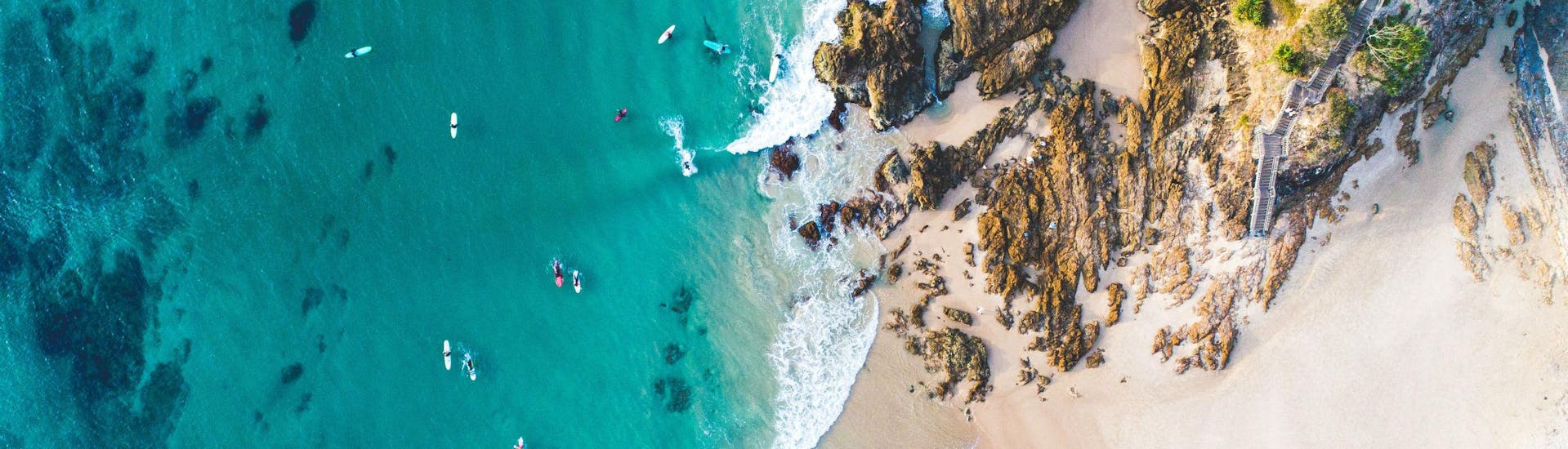 A bird's-eye view of several people paddling through the crystal clear waters along the coast while sea kayaking in Noosa.