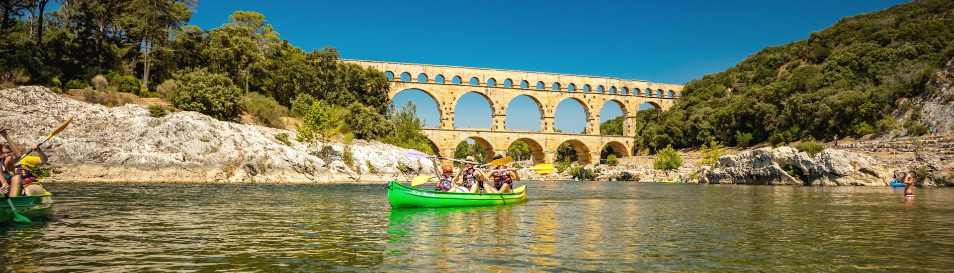 Dank Kayak Vert verbringt eine Familie einen schönen Tag beim Paddeln auf dem Gardon mit dem Pont du Gard, einem der beliebtesten Ziele für Kanutouren in Frankreich, im Hintergrund.