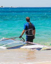 A young man is stood knee-deep in the sea with his board and sail, ready to go windsurfing in Naxos.