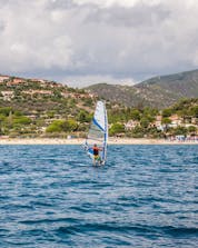 Un uomo dall'aspetto sportivo è raffigurato mentre fa windsurf vicino a Porto Pollo.