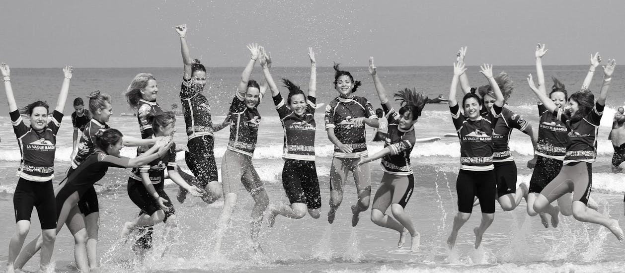 Des participants au cours de surf proposés par La Vague basque sur la plage de la Côte des Basques à Biarritz sautent dans les vagues sur le bord de la plage.