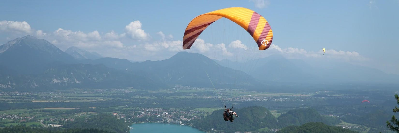 A pilot and a customer glide through the air together during tandem paragliding and enjoy the view of Lake Bled.
