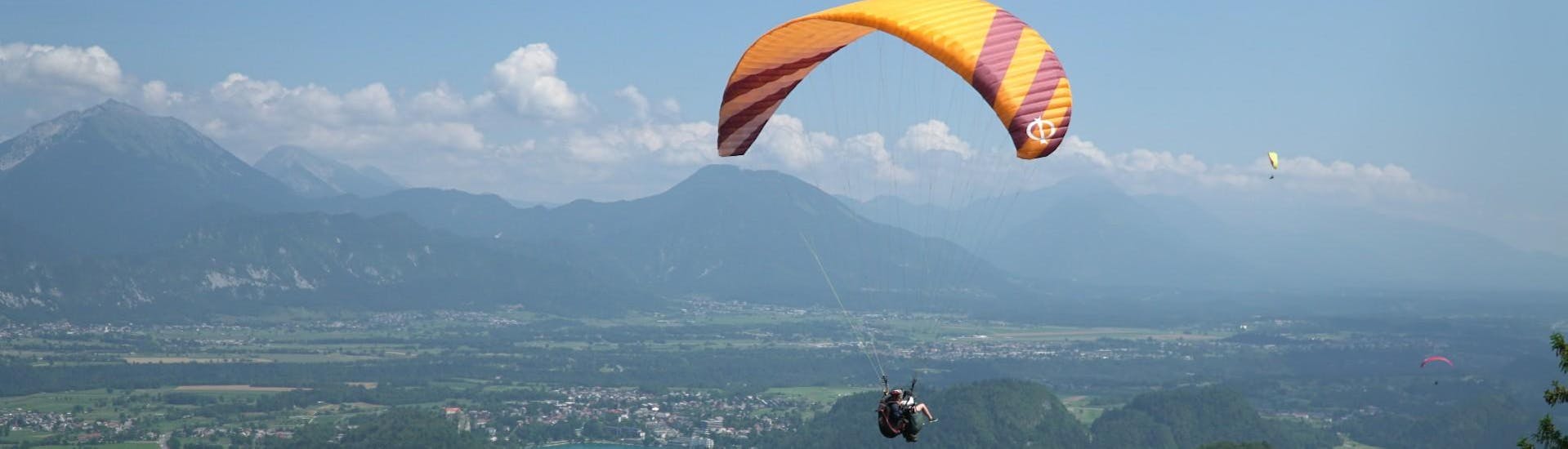 Ein Pilot und ein Kunde gleiten beim gemeinsamen Tandem Paragliding durch die Luft und genießen die Aussicht auf den Bleder See.