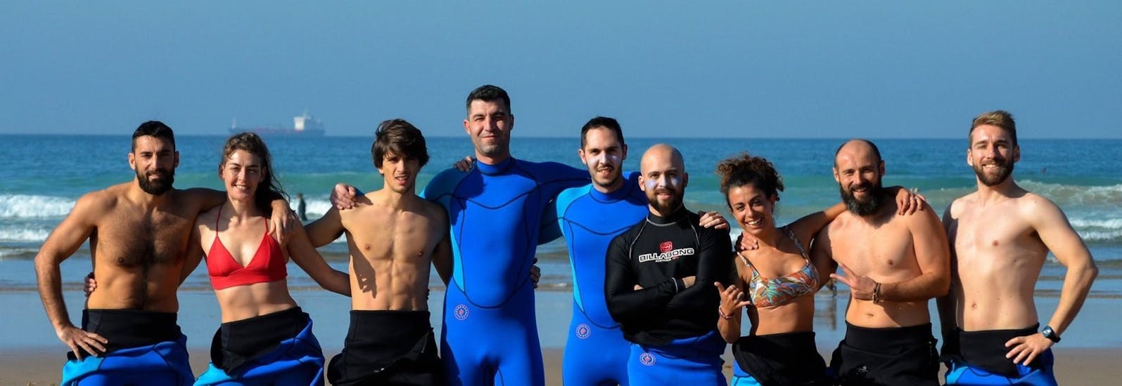 Eine Gruppe von Surfern steht gemeinsam mit ihren Surflehrern von Latas Surf am Strand und lächeln in die Kamera.