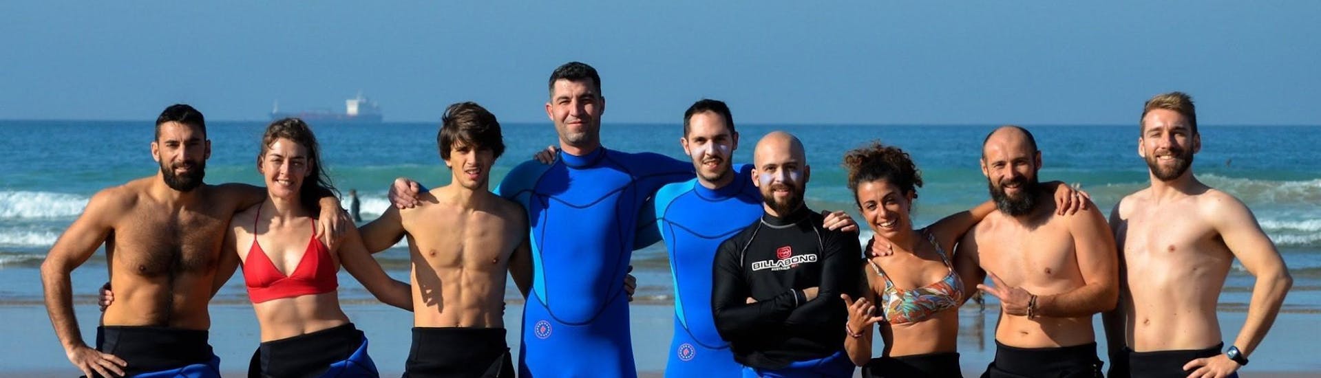 A group of surfers stands on the beach together with their surf instructors from Latas Surf and smile into the camera.