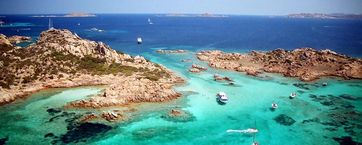 Immagine della costa rocciosa con acque color smeraldo e la barca de Le Meraviglie dell'Arcipelago in navigazione.