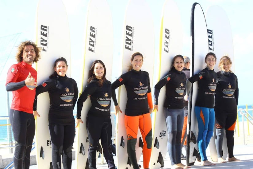A group of young women is posing for a group photo alongside their surf instructor from Lisbon Surfaris before they get started with their surf lesson.
