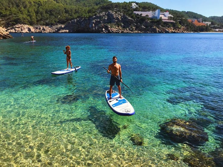Un hombre rema relajado por las aguas cristalinas y disfruta de la vista de las cuevas y bahías con Mediterrania Paddle Surf Ibiza. 