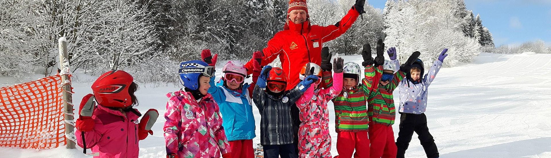 Skilehrer und Kinder mit erhobenen Händen bei der G&S Schneesportschule Mitterdorf.