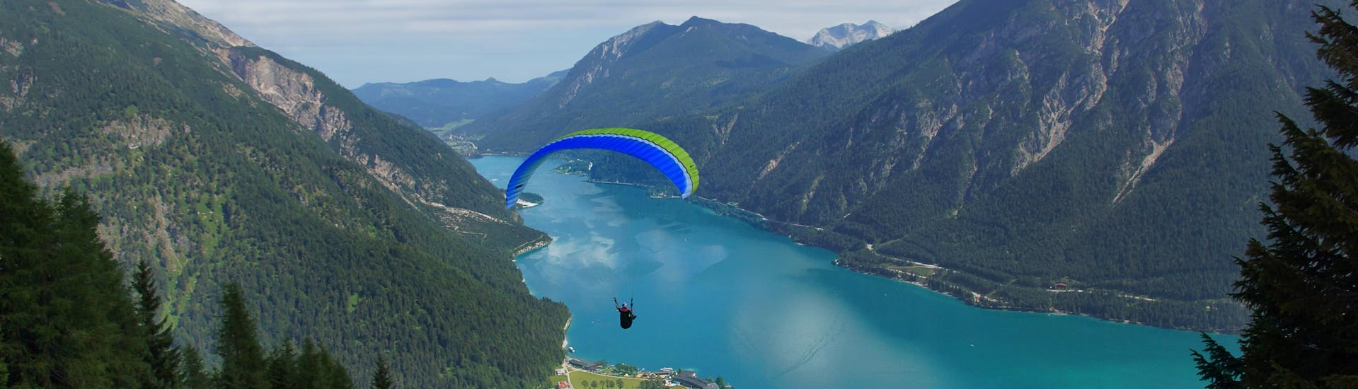 A tandem master and his passenger are sailing through cloudy skies while paragliding in Achensee.