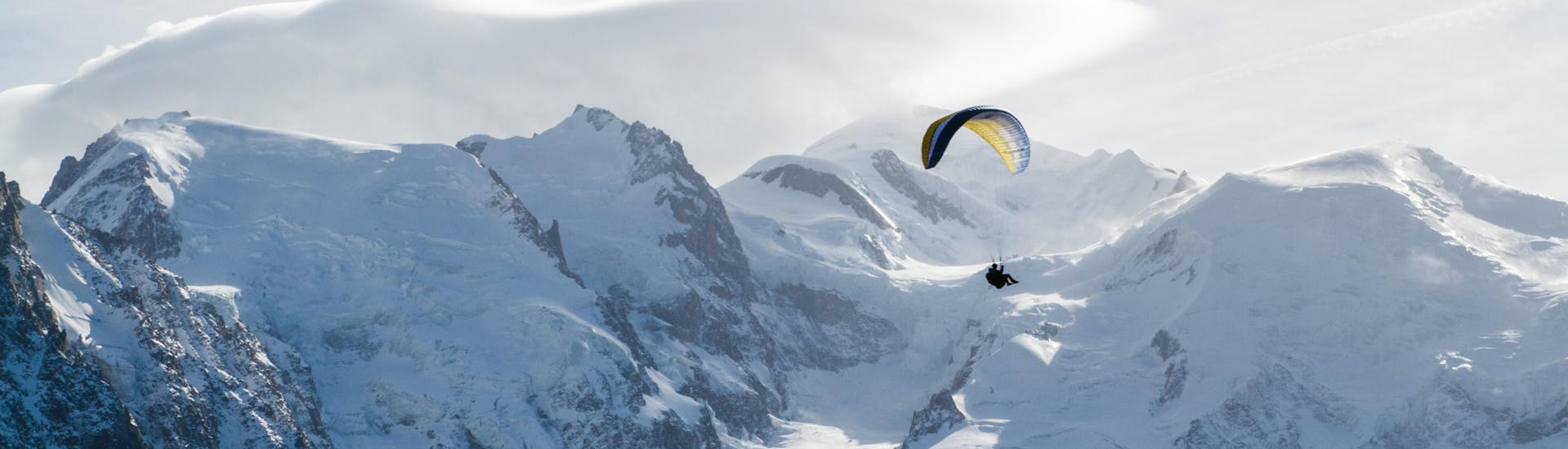 A person is doing a paragliding flight in the Chamonix valley from Aiguille du Midi with snowy mountains in the background.
