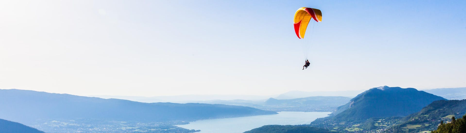 Ein Tandempilot und sein Passagier fliegen beim Paragliding in Lac d'Annecy sanft durch die Lüfte.