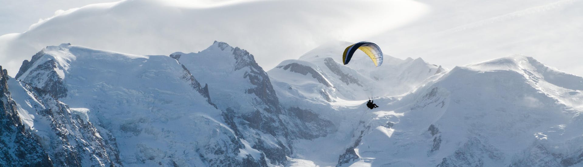 A person is doing a paragliding flight in the Chamonix valley with the snowy mountains in the background.
