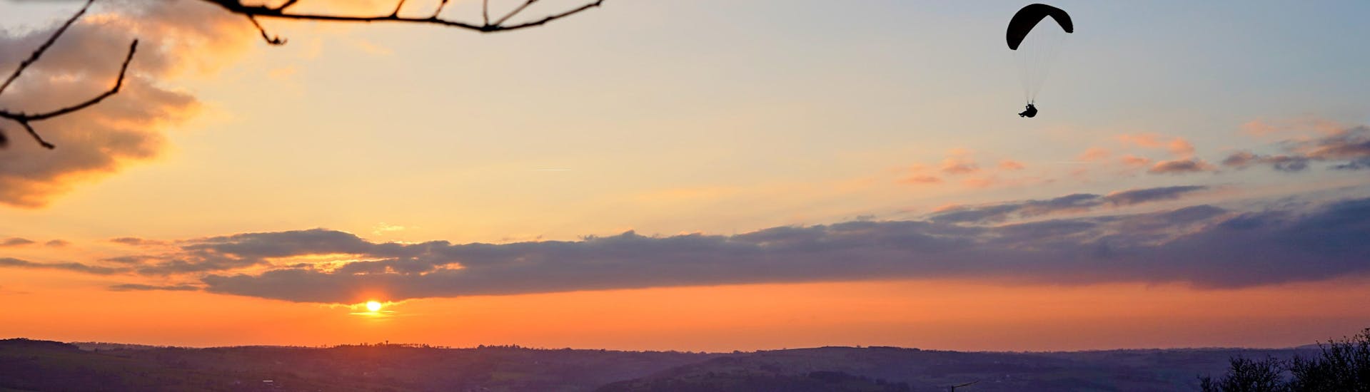 Un pilote de parapente effectue un vol en parapente au coucher du soleil au-dessus des paysages de Normandie à Clécy.