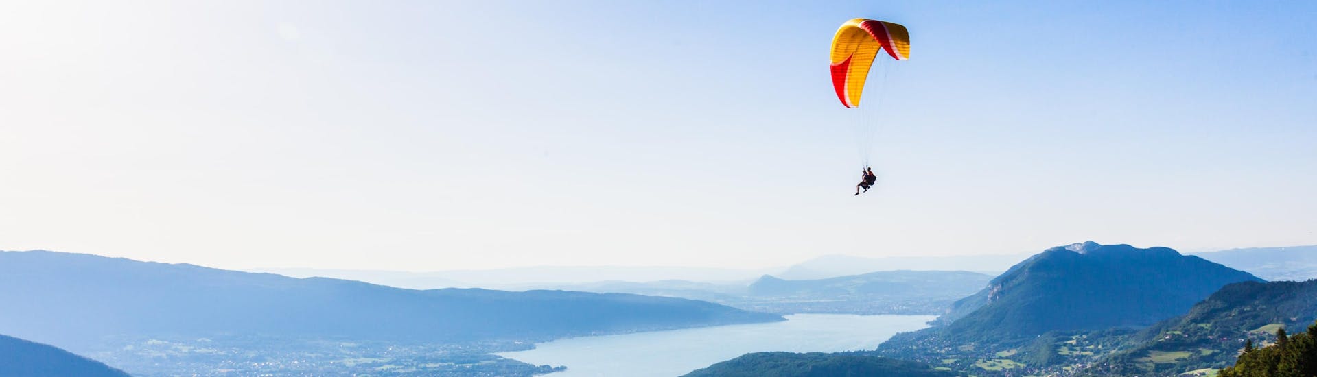A tandem master and their passenger are gently gliding over Lake Annecy while paragliding from Col de la Forclaz.