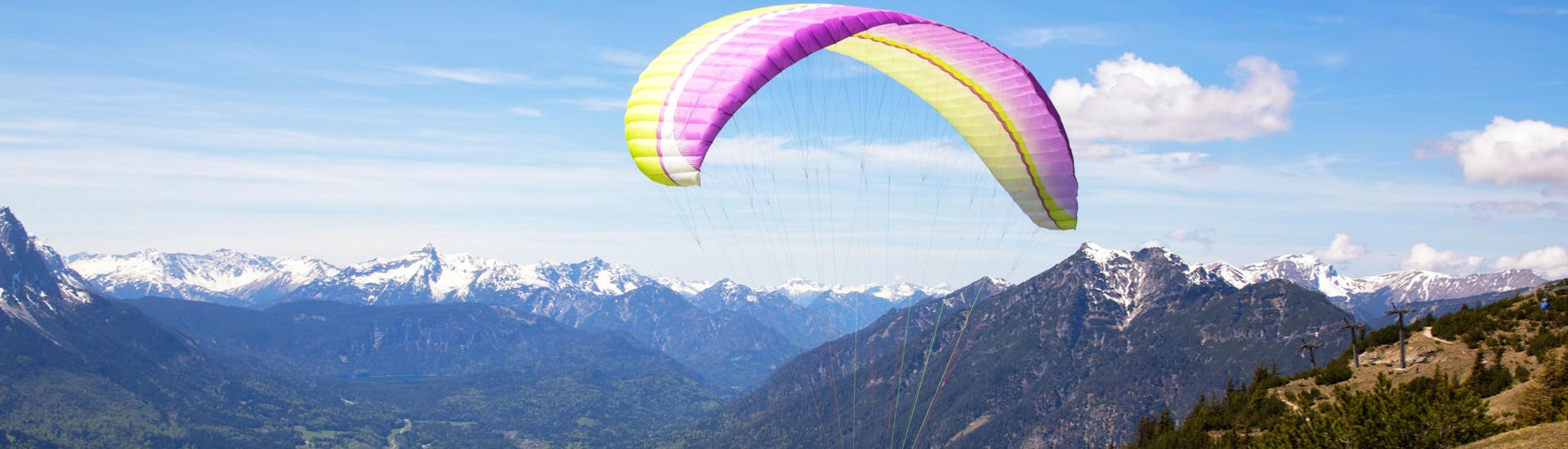 A tandem master and his passenger are sailing through cloudy skies while paragliding in Garmisch-Partenkirchen.