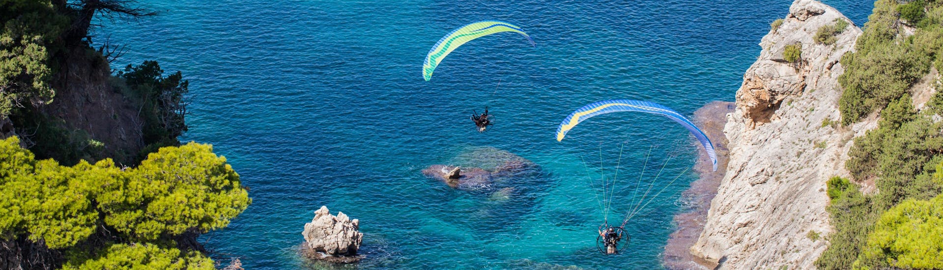 A tandem master and his passenger are sailing through cloudy skies while paragliding in Crete.