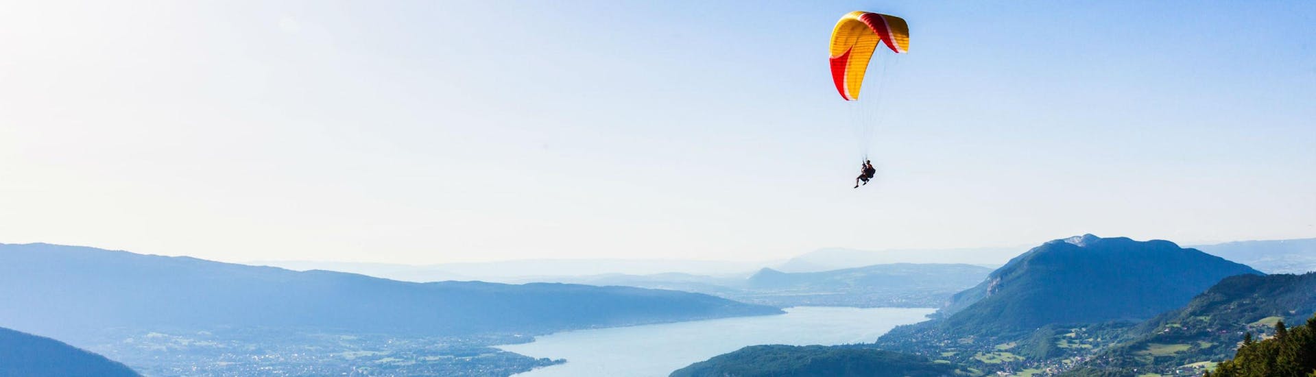Un pilote de tandem et son passager planent doucement dans le ciel en faisant du parapente au-dessus du lac d'Annecy.