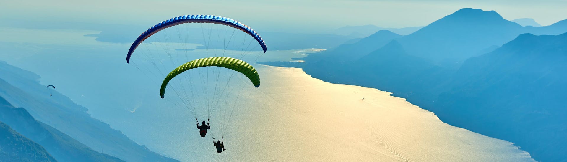 A tandem master and his passenger are sailing through cloudy skies while paragliding in Malcesine.