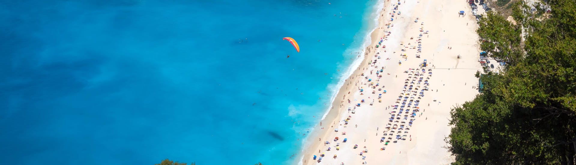 Un entusiasmado participante en un vuelo en parapente biplaza sobrevuela Playa de Myrtos, uno de los sitios más populares para volar en parapente.