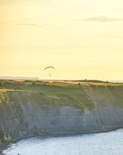 A tandem pilot and his passenger can be seen flying above a cliff while paragliding in Normandy.