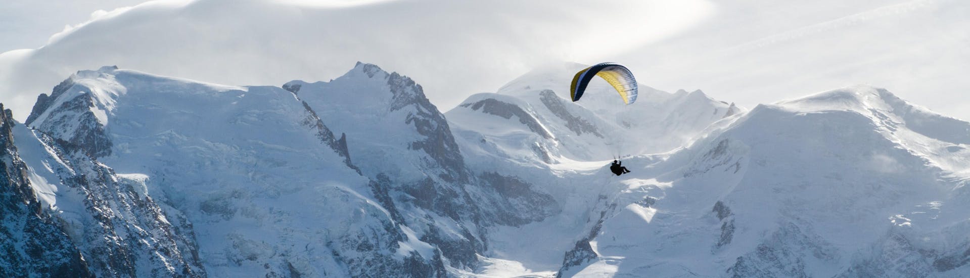 A person is doing a paragliding flight in the Chamonix valley from Plan Praz with the snowy mountains in the background.