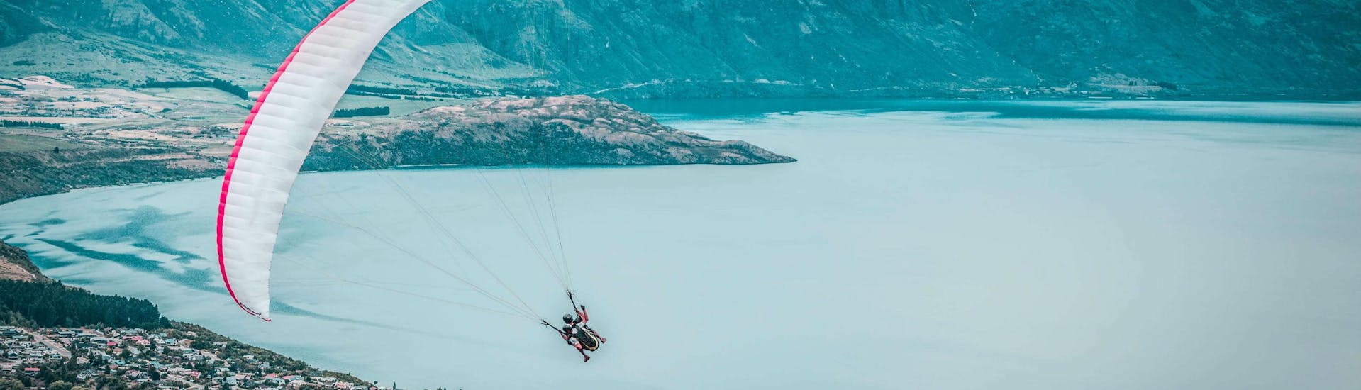 A tandem master and his passenger are flying over Lake Wakatipu while paragliding in Queenstown, New Zealand.