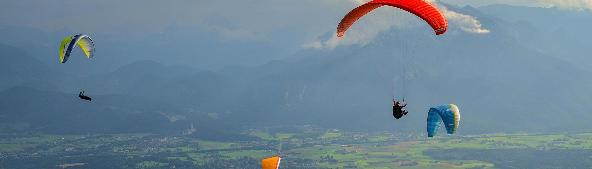 A tandem master and his passenger are sailing through cloudy skies while paragliding in Salzburg.