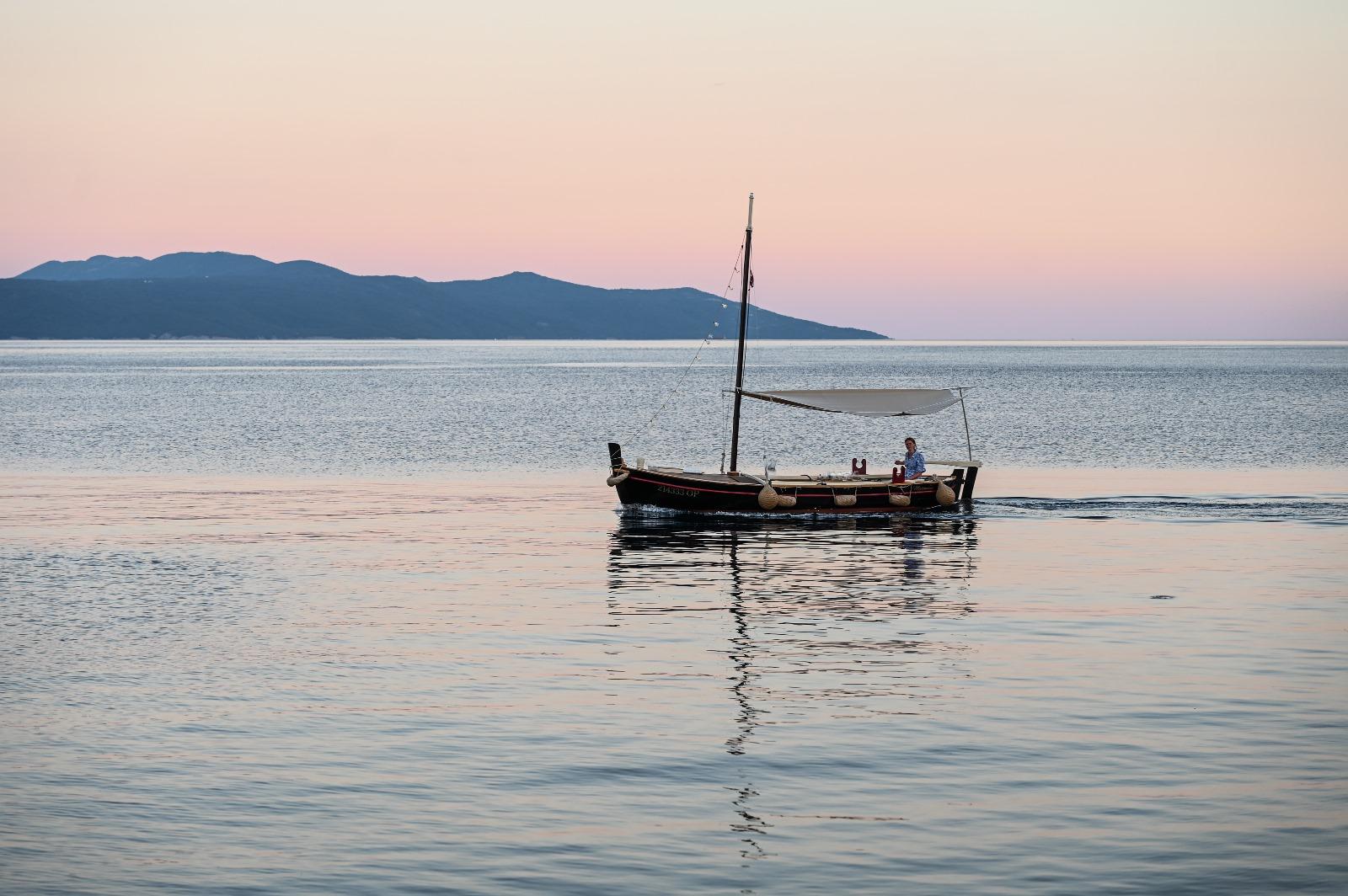 Barco tradicional croata de madera del Madonnina en Opatija sobre el agua durante la puesta de sol.