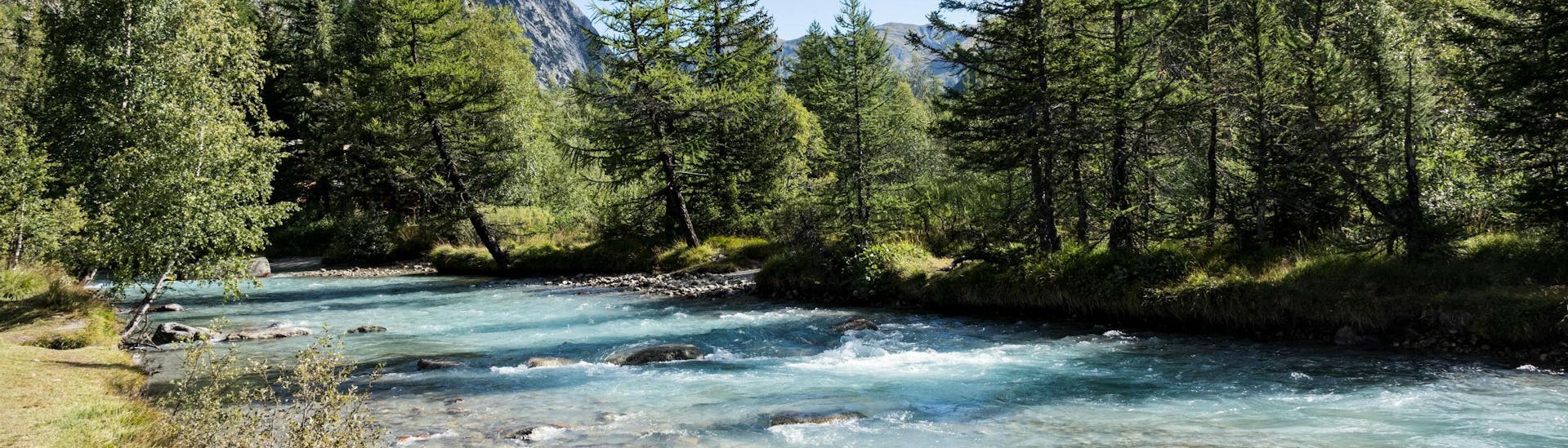 An image of a river flowing through the picturesque mountain scenery that people who go rafting in Aosta Valley get to experience.