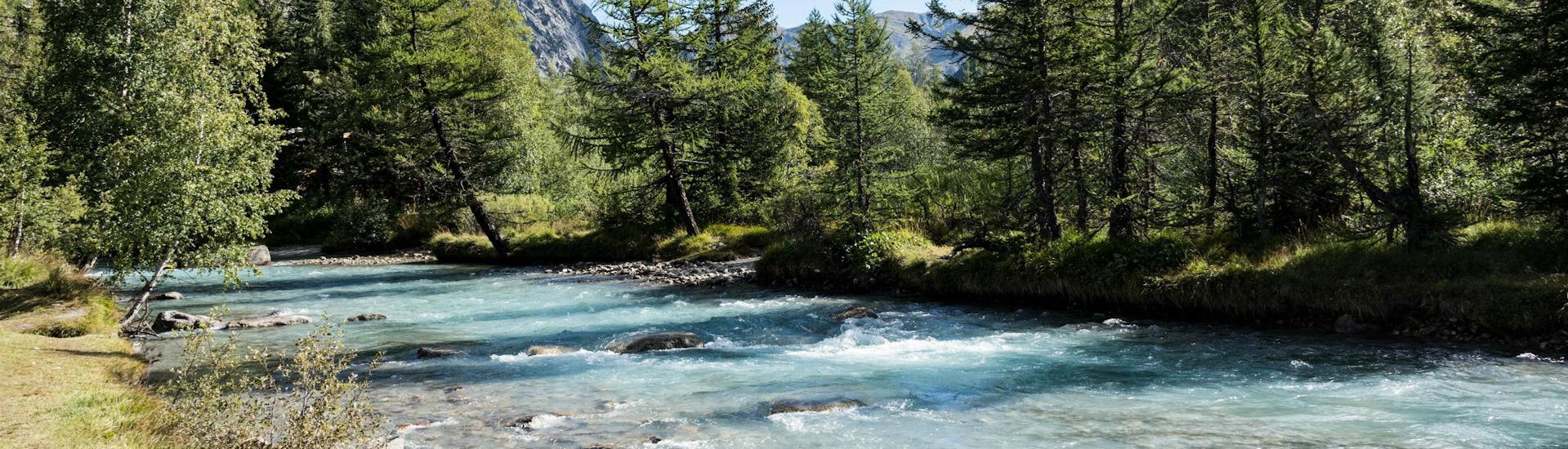 An image of a river flowing through the picturesque mountain scenery that people who go rafting in Aosta Valley get to experience.