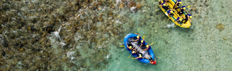 Two groups of people are paddling across the crystal clear waters of the Soca River while rafting in Bovec.