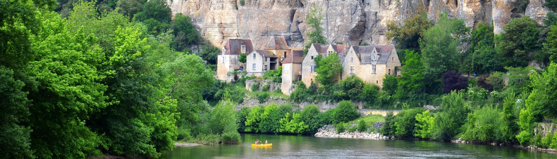 Des amateurs de canoë pagayent tranquillement sur la Vézère en Dordogne devant les habitats troglodytiques de la commune de Les Eyzies.