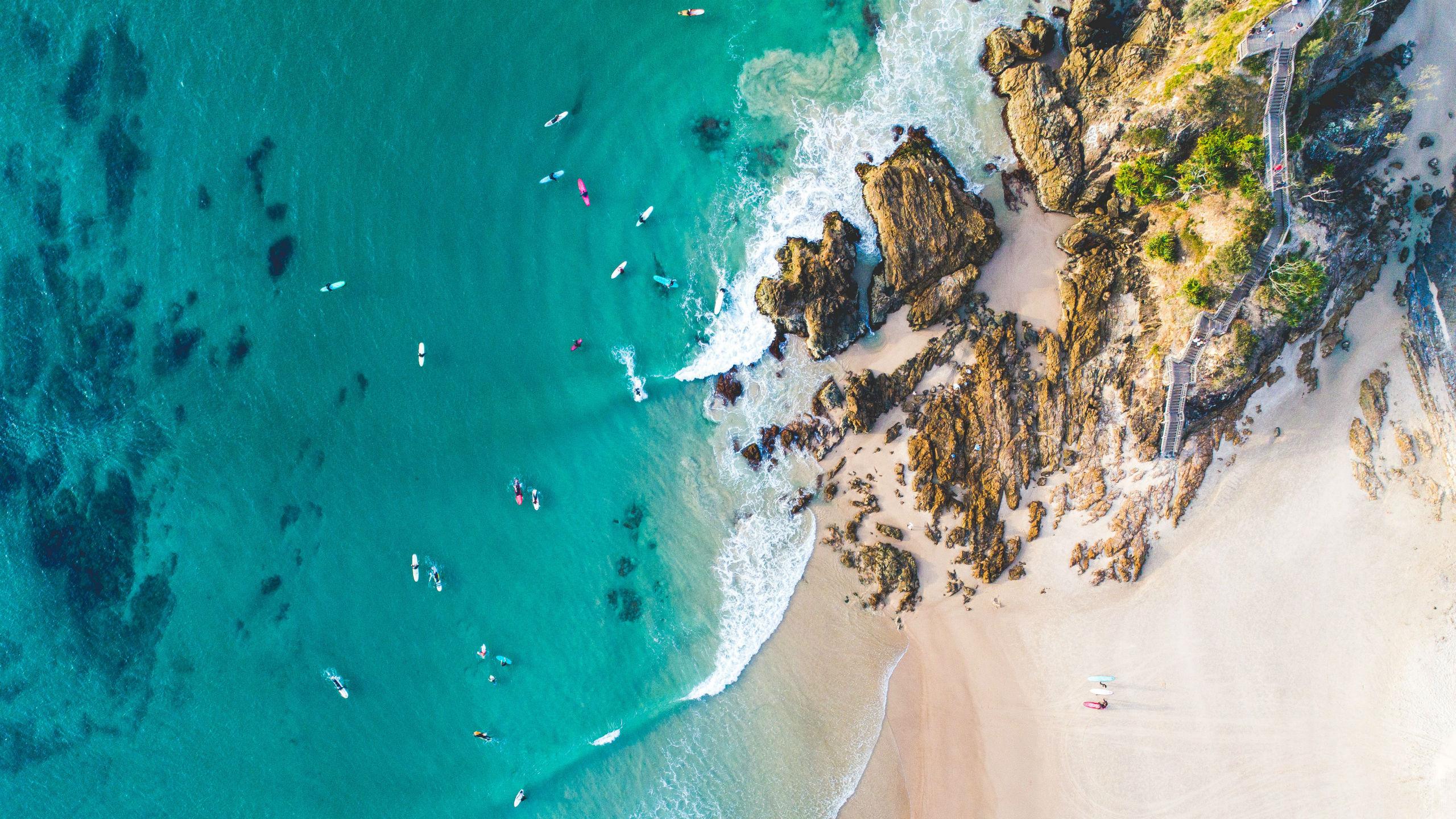 A bird's-eye view of several people paddling through the crystal clear waters along the coast while sea kayaking in Noosa.