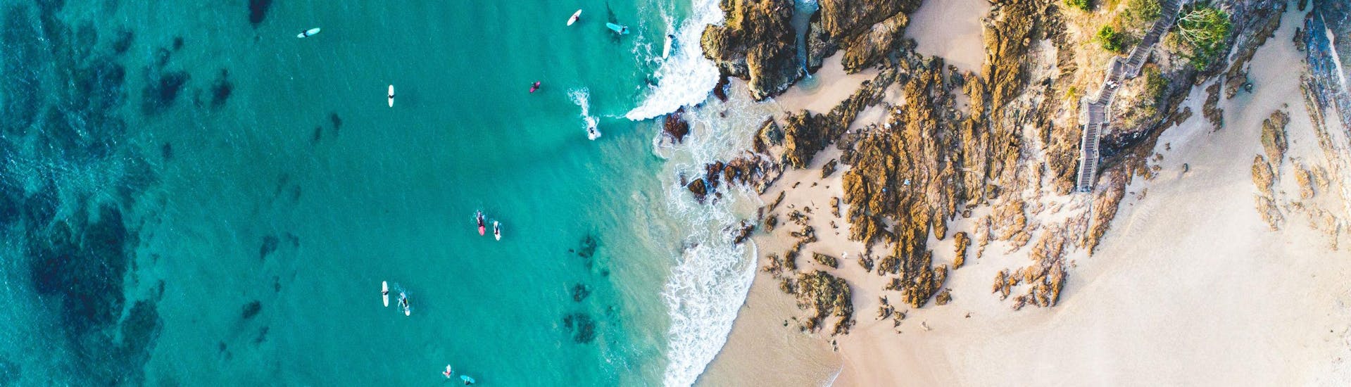 A bird's-eye view of several people paddling through the crystal clear waters along the coast while sea kayaking in Noosa.