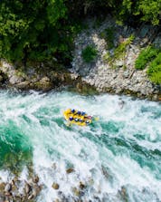 A group of people is pictured from above as they navigate their boat across the rapids while rafting in Valsesia.