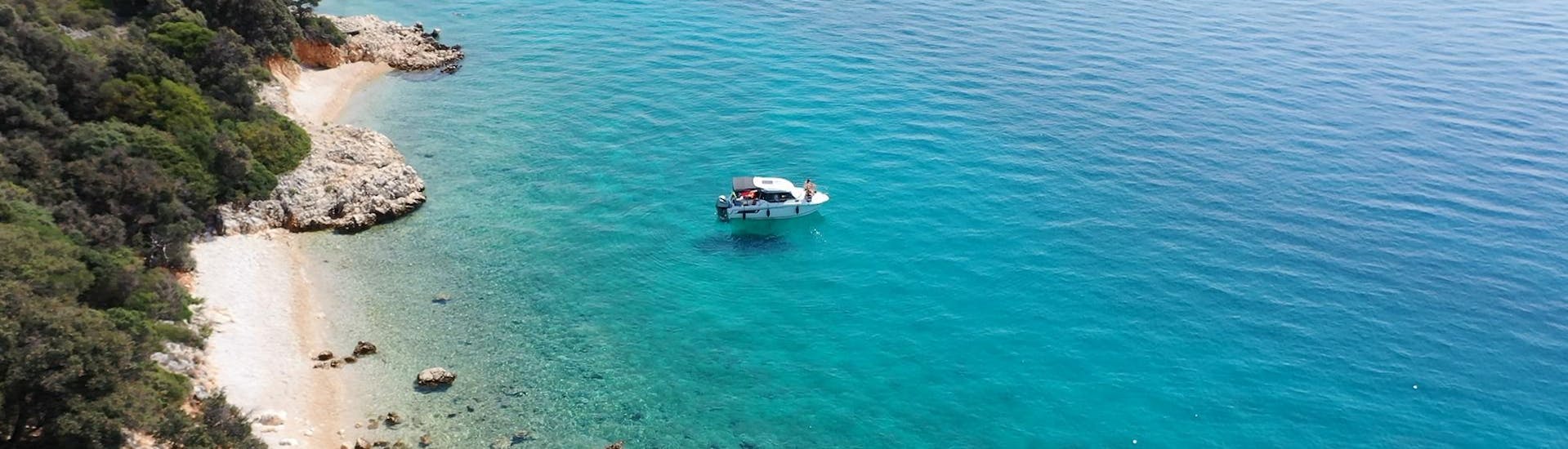 Ein Boot von Rent a Boat & Jetski Krk vor einem Strand im türkisen Wasser.