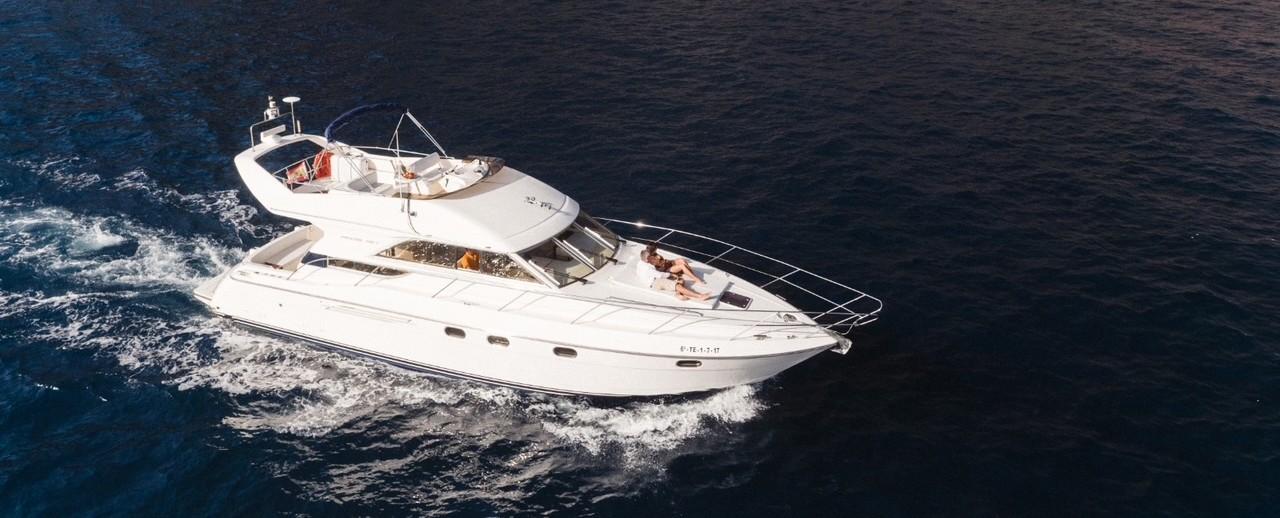 Ein privater, luxuriöser Yachtcharter von Royal Ocean Las Galletas gleitet durchs Wasser vor Teneriffa, während Touristen an Deck entspannen und ein Sonnenbad nehmen.
